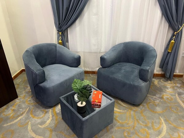 A room with two blue armchairs, a small black coffee table with a plant and a box, and a patterned carpet. - agnehat alsmo hotel (Abu Arish)