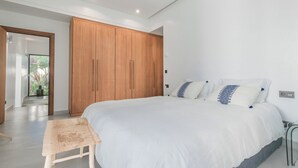 Un dormitorio moderno con una cama grande, un armario de madera y un pequeño banco de madera.