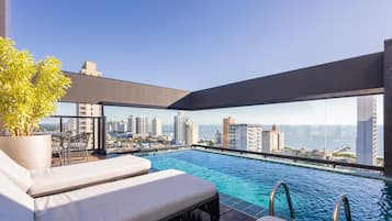 A rooftop infinity pool with a city view, lounge chairs, and a potted plant.