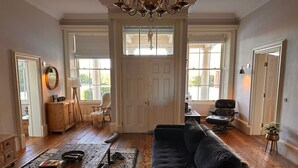 Ein geräumiges Wohnzimmer mit einer dunklen Couch, Holzböden und einem großen Fenster.