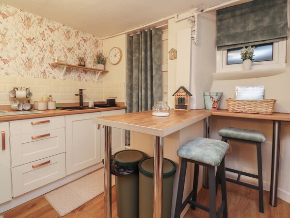 A compact kitchen with white cabinets, a wooden countertop, and a small stool. - Willow Wood (Settle)