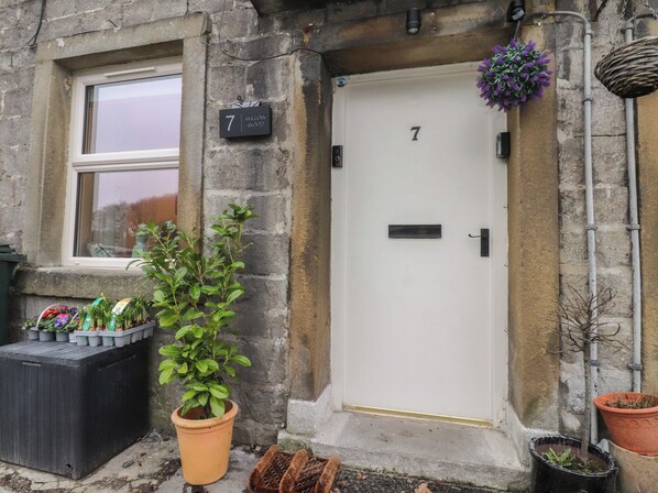 A stone building with a white door marked with the number 7, a small window, and a potted plant in front. - Willow Wood (Settle)