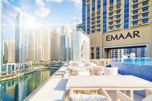 A rooftop pool area with lounge chairs and a view of the city skyline, including the Emaar building. - LUX The JW Marina Suite 5 (Dubai)