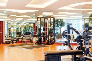 Een moderne sportschool met diverse gewichthefapparaten, een bank en een spiegelwand die de apparatuur en ramen weerspiegelt.