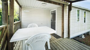 Un espacio al aire libre cubierto con una mesa y sillas blancas, una terraza de madera y una puerta que da a una casa.