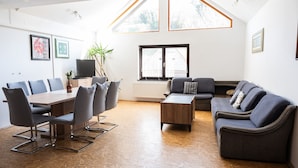 Un grand espace de vie doté d’un plafond haut, d’une table à manger avec des chaises, d’un canapé et d’un téléviseur.