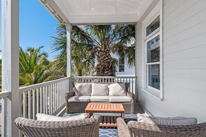 Eine überdachte Veranda mit Korbmöbeln, einer Palme und einem weißen Geländer.