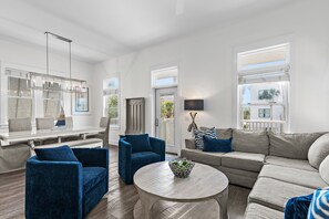 Ein modernes Wohnzimmer mit einem Ecksofa, einem blauen Sessel, einem runden Couchtisch und einem Essbereich mit Tisch und Stühlen.
