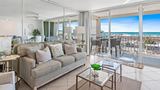 Uma sala de estar moderna com um sofá cinzento, mesa de centro de vidro e vista para a praia.