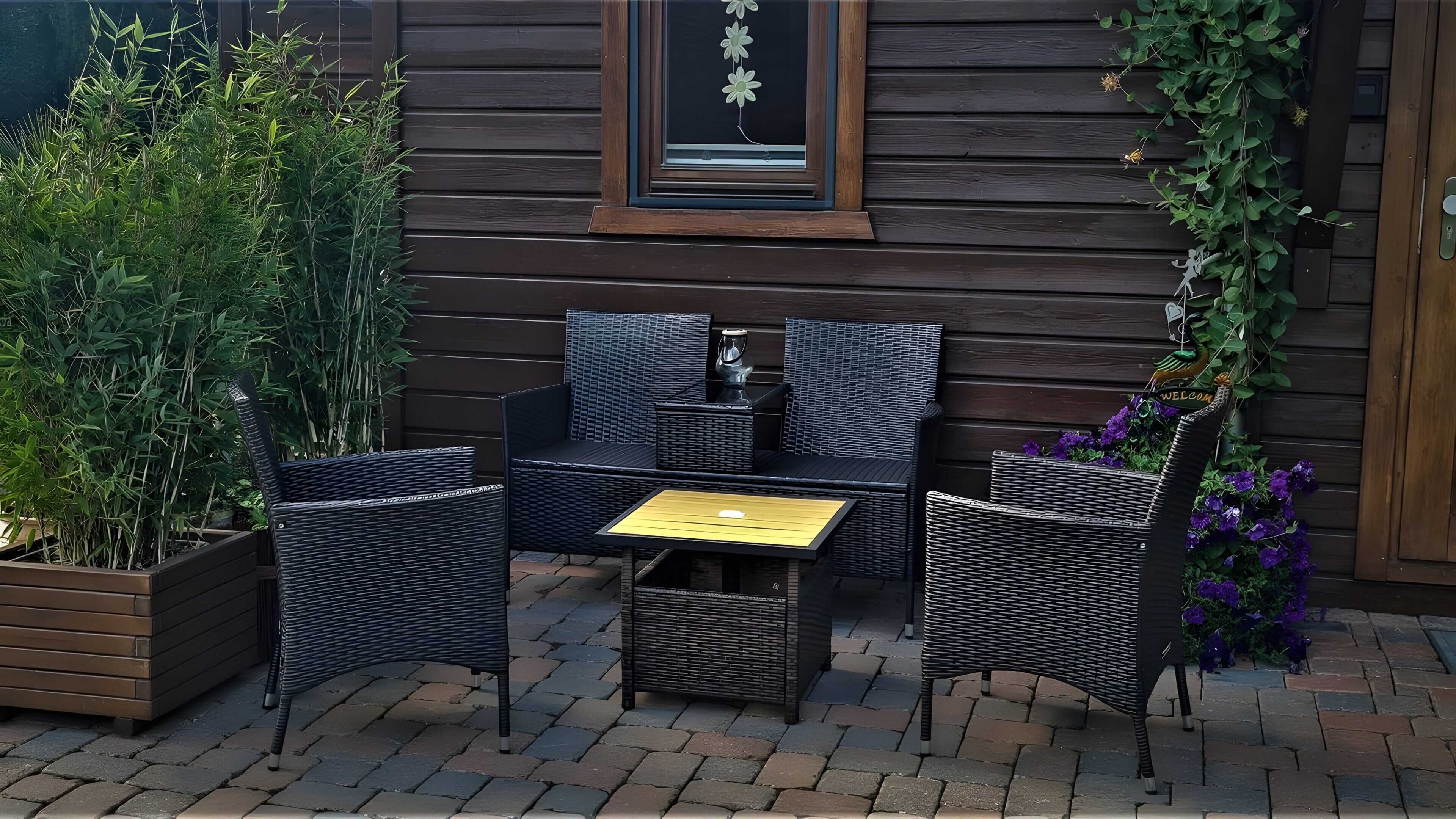 Un área de estar al aire libre con mobiliario de mimbre, una mesa de madera y una ventana con una flor decorativa.