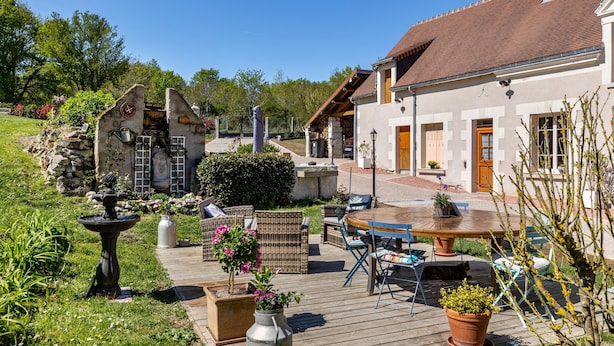 Une terrasse avec des meubles d’extérieur, une fontaine en pierre et des plantes en pot.