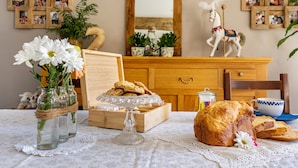Une table à manger avec une miche de pain, une assiette de biscuits et un vase de fleurs.