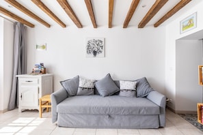 Een kamer met een grijze bank, een wit kastje en een plafond met houten balken.