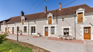 Une rangée d’immeubles à deux étages, tous de style architectural uniforme, avec des fenêtres et des portes disposées de manière symétrique, une allée gravillonnée et des espaces de détente en plein air.