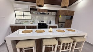 A modern kitchen with a large island, wooden bar stools, and pendant lighting.