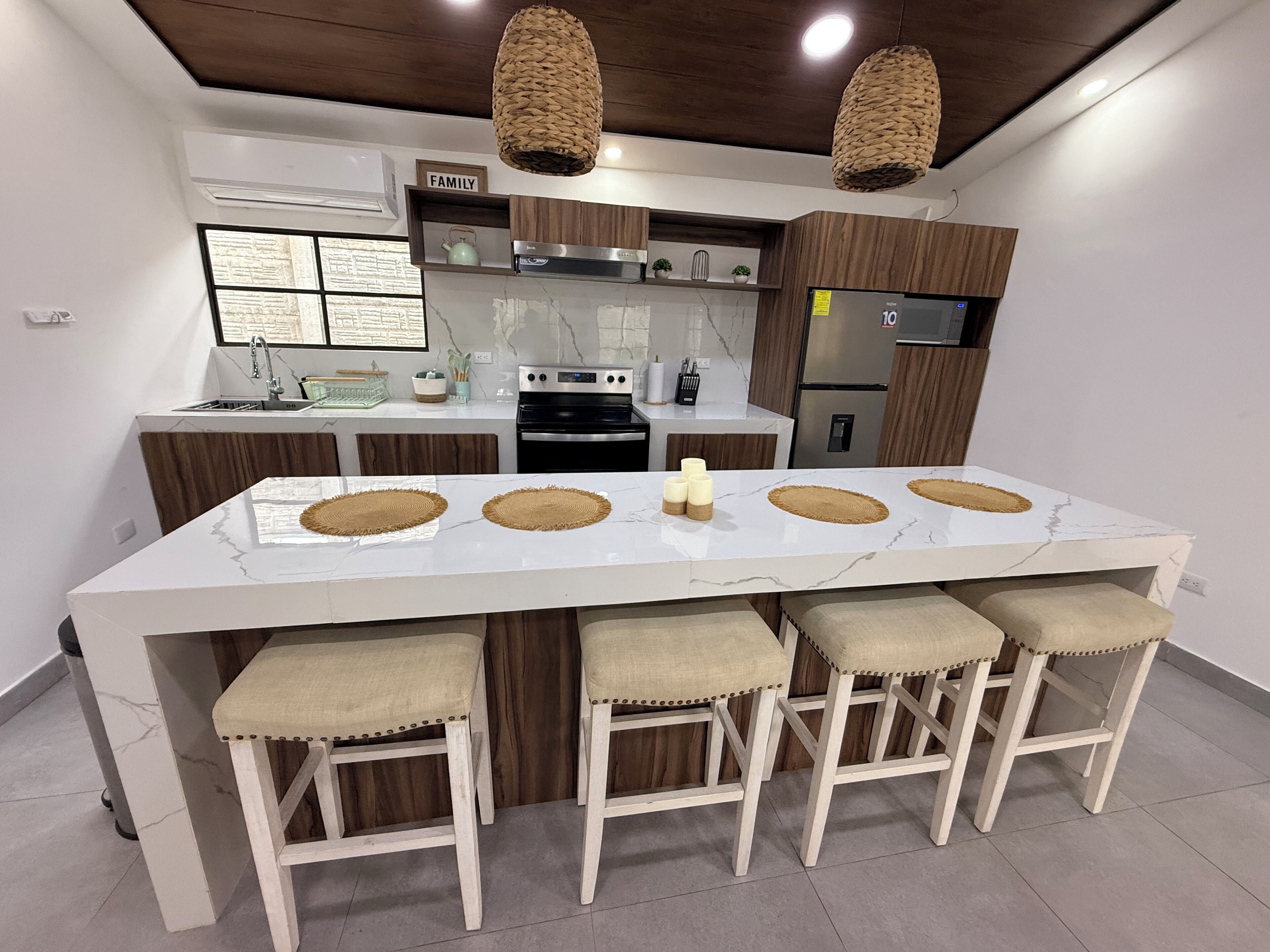 A modern kitchen with a large island, wooden bar stools, and pendant lighting.