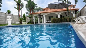A swimming pool with a covered patio area, white columns, and outdoor seating.