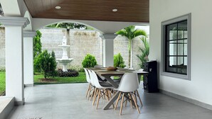 A covered patio with a dining table, chairs, a stone wall, and a fountain.