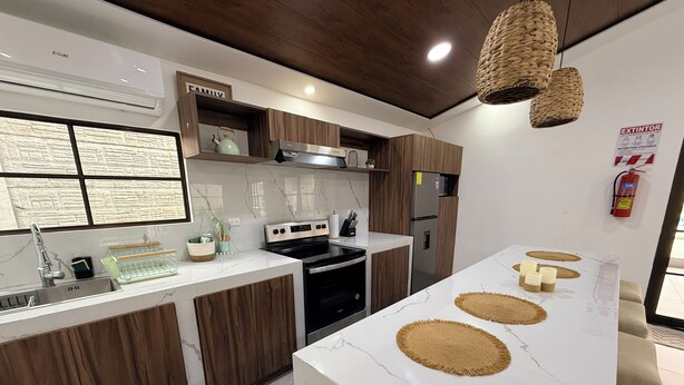 A modern kitchen with a central island, wooden cabinets, a stainless steel refrigerator, and a built-in oven.