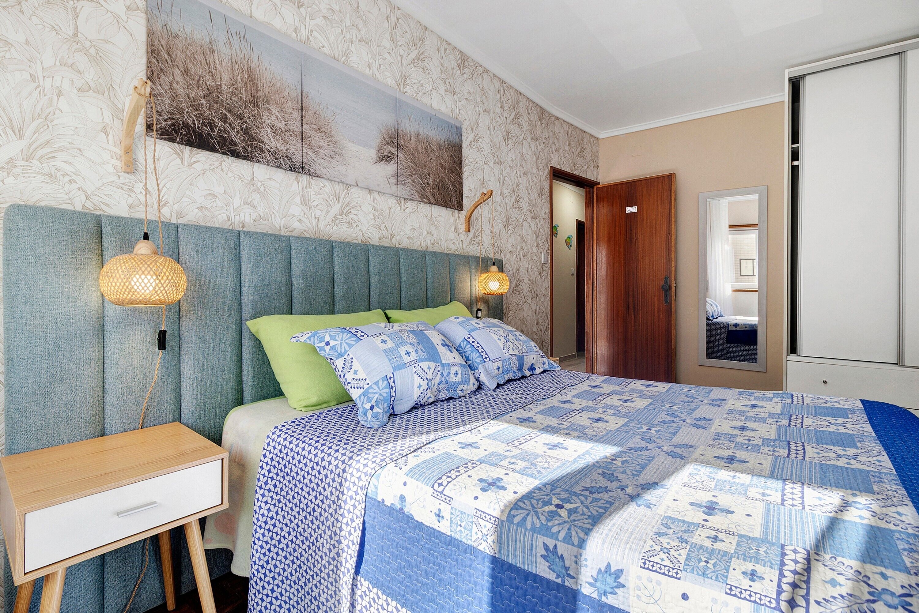 A bedroom with a bed, a nightstand, a wall-mounted lamp, and a painting.