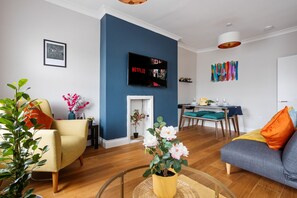 A modern living room with a blue accent wall, a flat-screen TV, a fireplace, and a dining area with a table and chairs. - Vibrant & Stylish|2BR|Shepherd’s Bush|Fast WiFi|ST (Greater London)