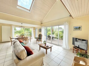 A spacious living room with a high ceiling, a large window, and a sliding glass door leading to an outdoor area. - The bread oven. Country house 10 minutes from downtown Quimper. Sleeps 8. (Pluguffan)