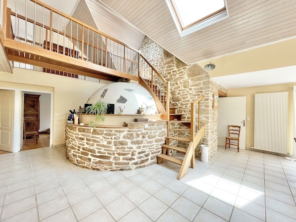 A spacious living area with a stone fireplace, wooden staircase, and a mezzanine level. - The bread oven. Country house 10 minutes from downtown Quimper. Sleeps 8. (Pluguffan)