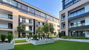 En modern lägenhetsbyggnad med flera balkonger, en central innergård med konstgräs och diverse krukväxter.