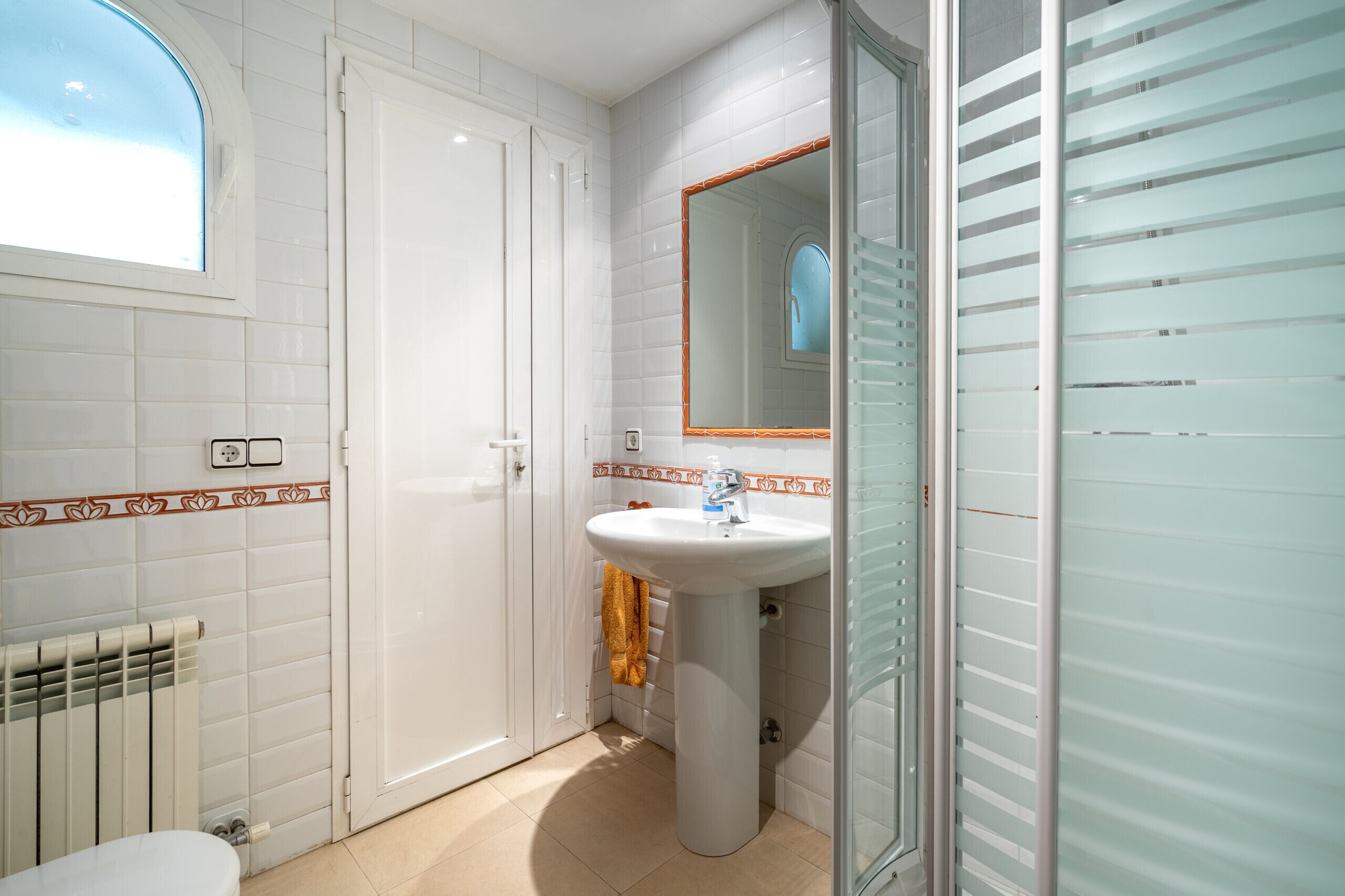 A bathroom with white tiled walls, a white sink with a mirror, and a towel hanging on the wall.