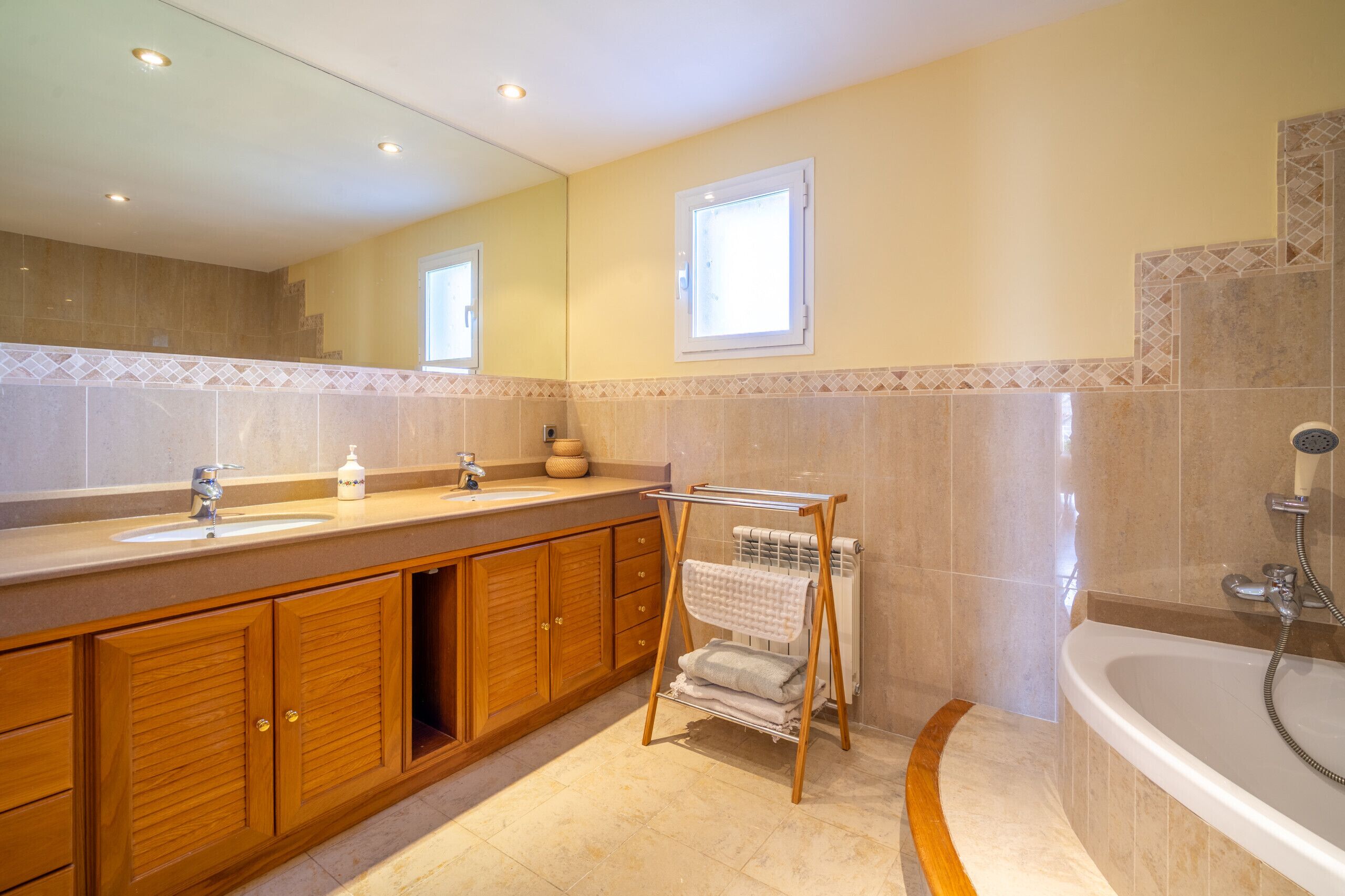 A bathroom with a large mirror, wooden cabinets, a sink, a bathtub, and a towel rack.