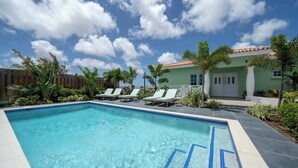 A swimming pool with clear blue water, surrounded by lounge chairs and palm trees. - Modern Apt w/ Sea View & Pool | Jan Thiel (Willemstad)