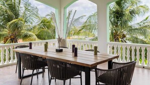 A wooden table with chairs, a white railing, and palm trees in the background. - Modern Apt w/ Sea View & Pool | Jan Thiel (Willemstad)