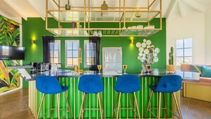 Een keuken met een groen kookeiland, barstoelen, een flatscreen televisie en een koelkast.