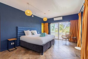 A bedroom with a bed, a small table, a chair, and a balcony with curtains. - Modern Villa w/ Sea View & 2 Pools | Jan Thiel (Willemstad)