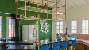 Una cucina moderna con una parete verde a contrasto, un'area bar con sedie blu e una zona salotto con un divano.