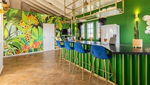 Una cucina con una parete verde a contrasto, una zona bar con sedie blu e un murale con motivo leopardato.