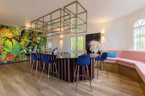 A modern kitchen with a bar area, bar stools, a pink sofa, and a mural of tropical leaves. - Modern Apt w/ Plunge Pool | Jan Thiel (Willemstad)