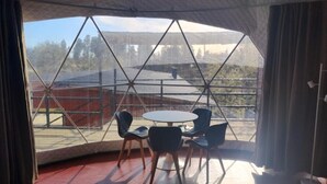 Een kamer met een groot raam dat uitzicht biedt op een bergachtig landschap. Binnenin staat een ronde tafel met vier stoelen.