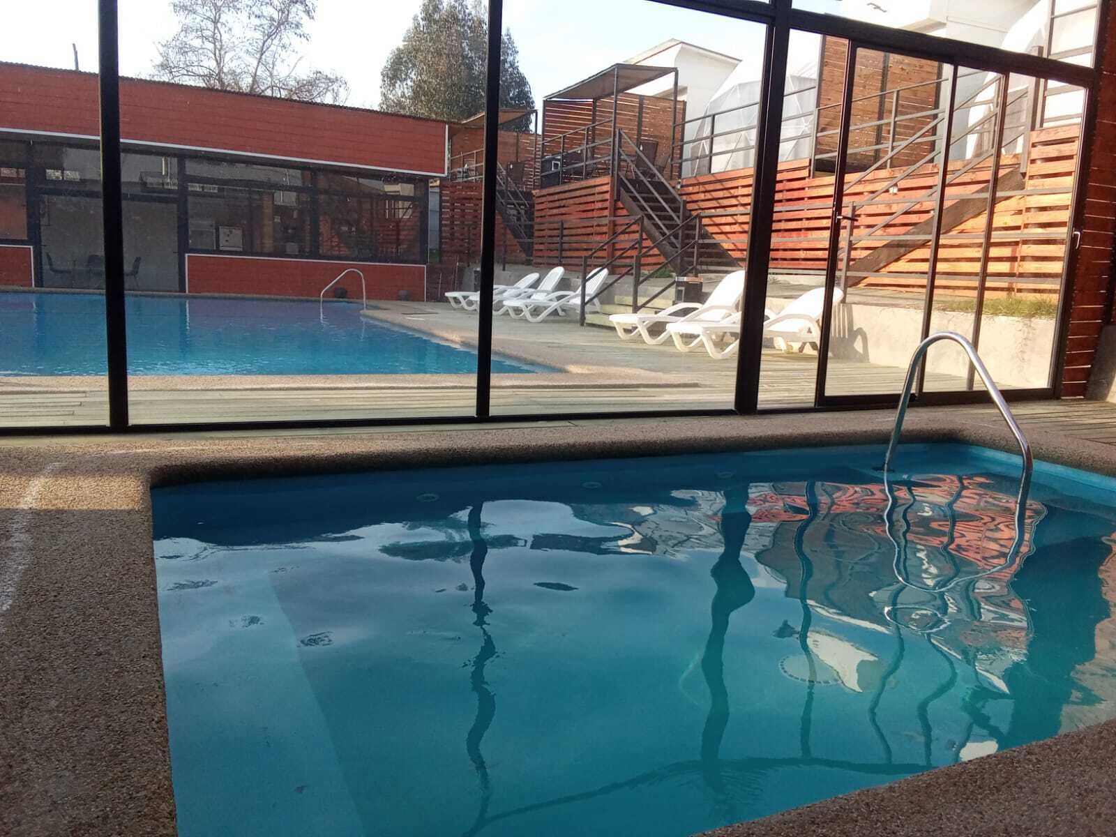 Una piscina con una escalera de metal, rodeada por un cerramiento de vidrio.