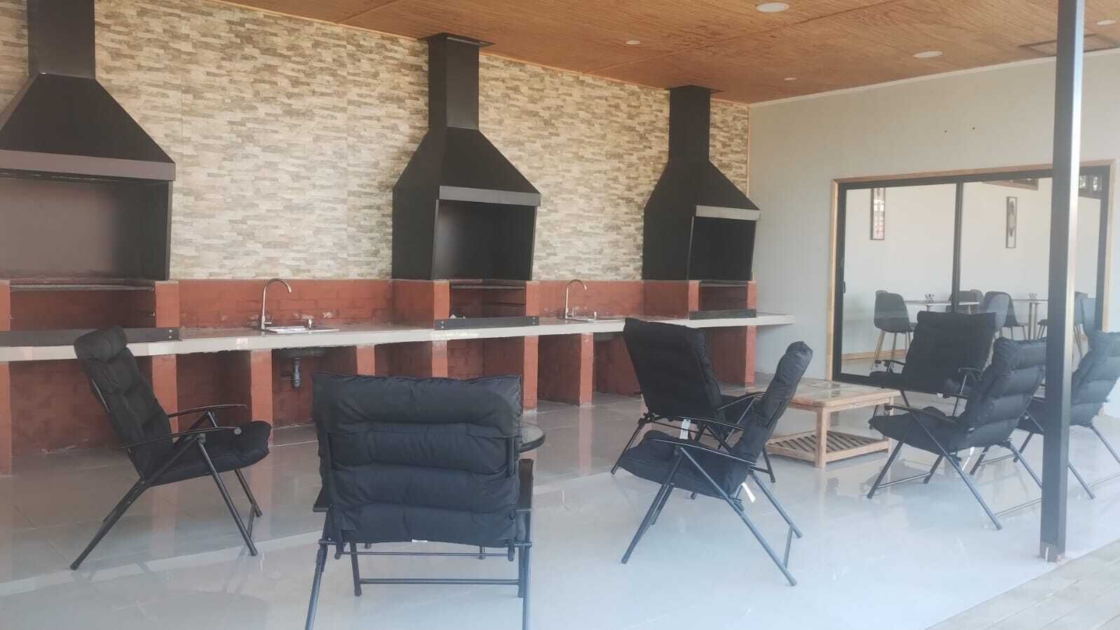 A modern indoor seating area with black chairs and a long table, a stone wall, and three black chimneys.