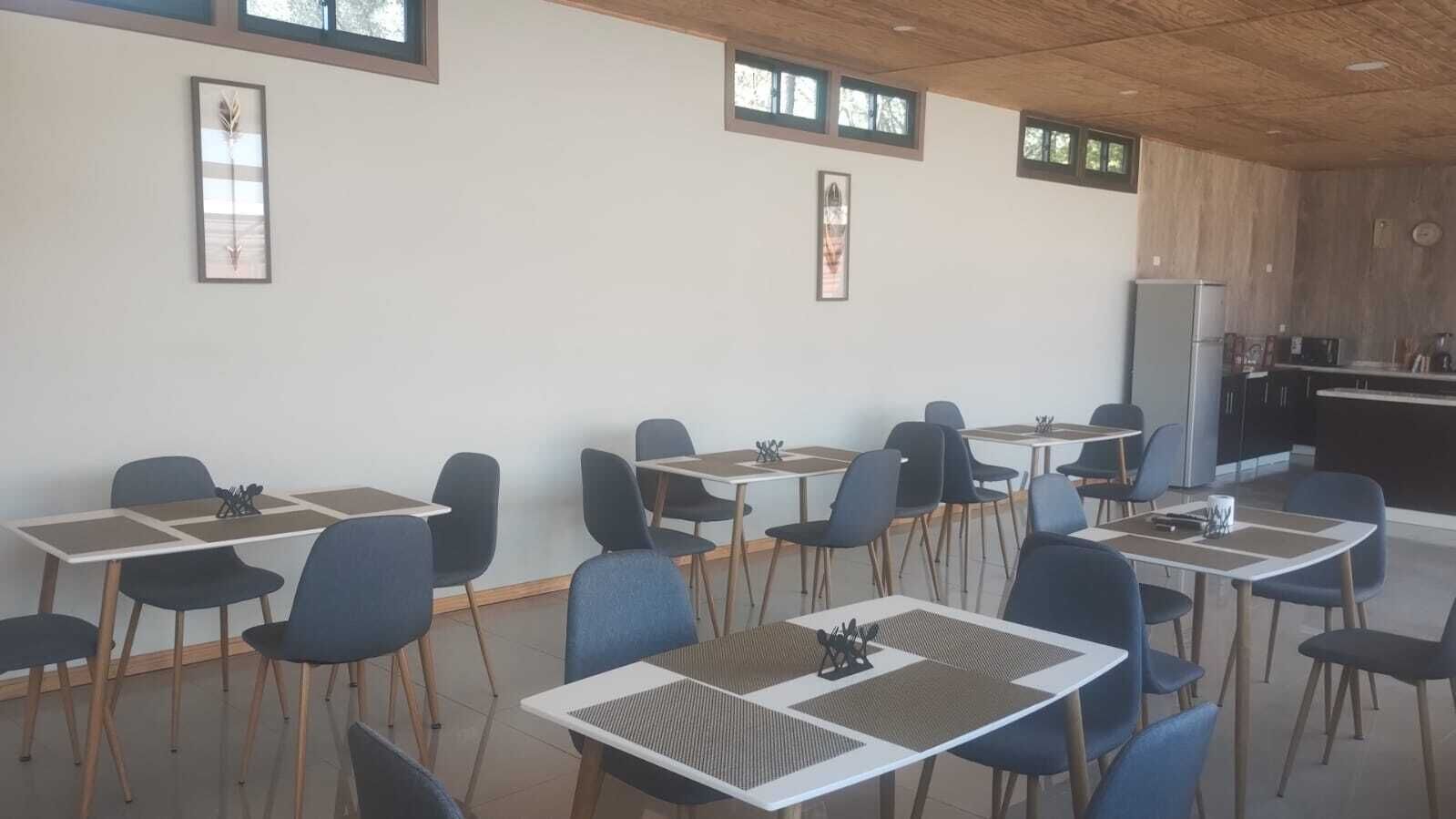 Een eethoek met tafels en stoelen, een keuken op de achtergrond, en lijstjes met foto's aan de muren.