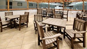 A covered outdoor dining area with wooden tables and chairs, a tiled floor, and a view of a building in the background. - Myrtle Beach Resort FS4106 (Myrtle Beach)