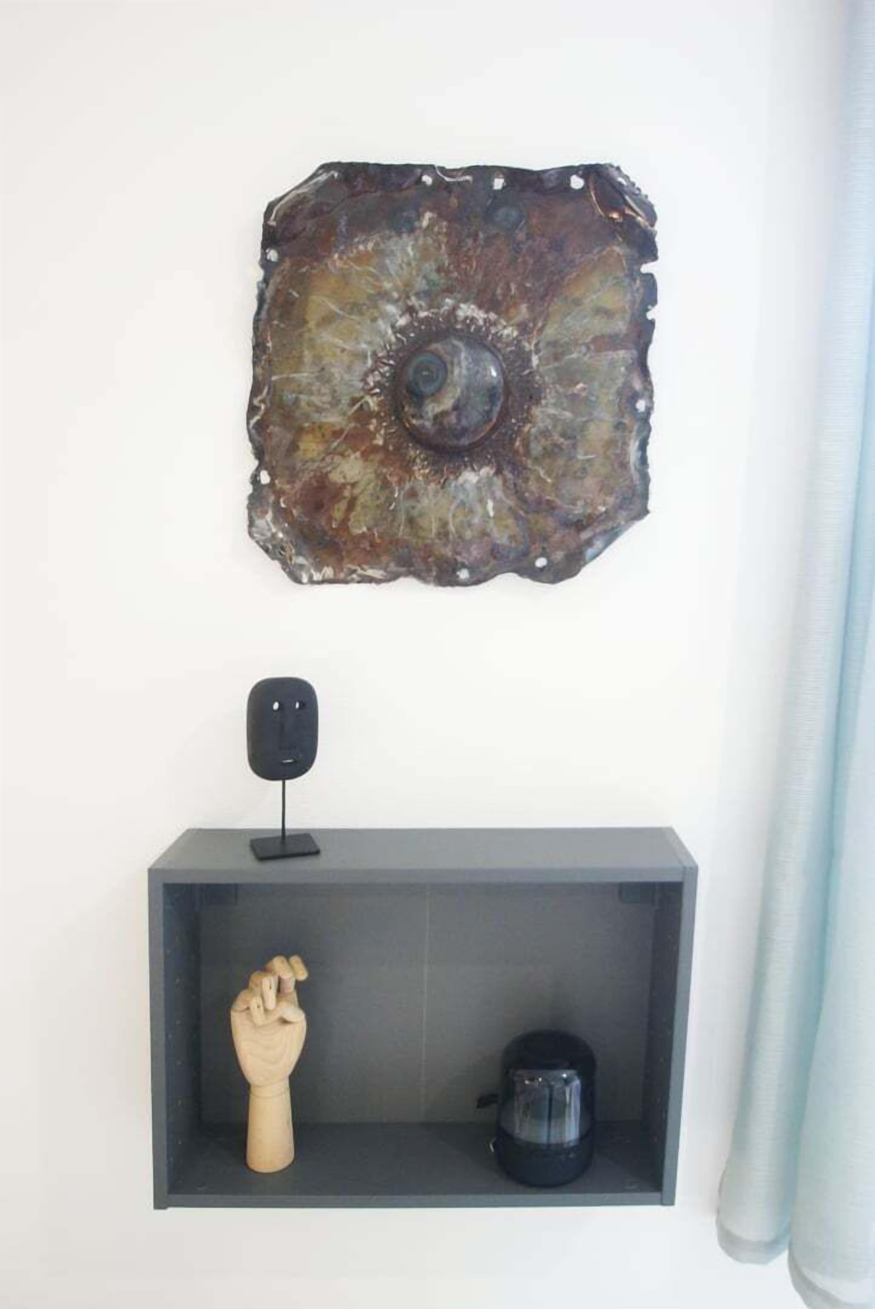 A wall-mounted abstract metal artwork, a black speaker on a shelf, and a wooden hand sculpture.