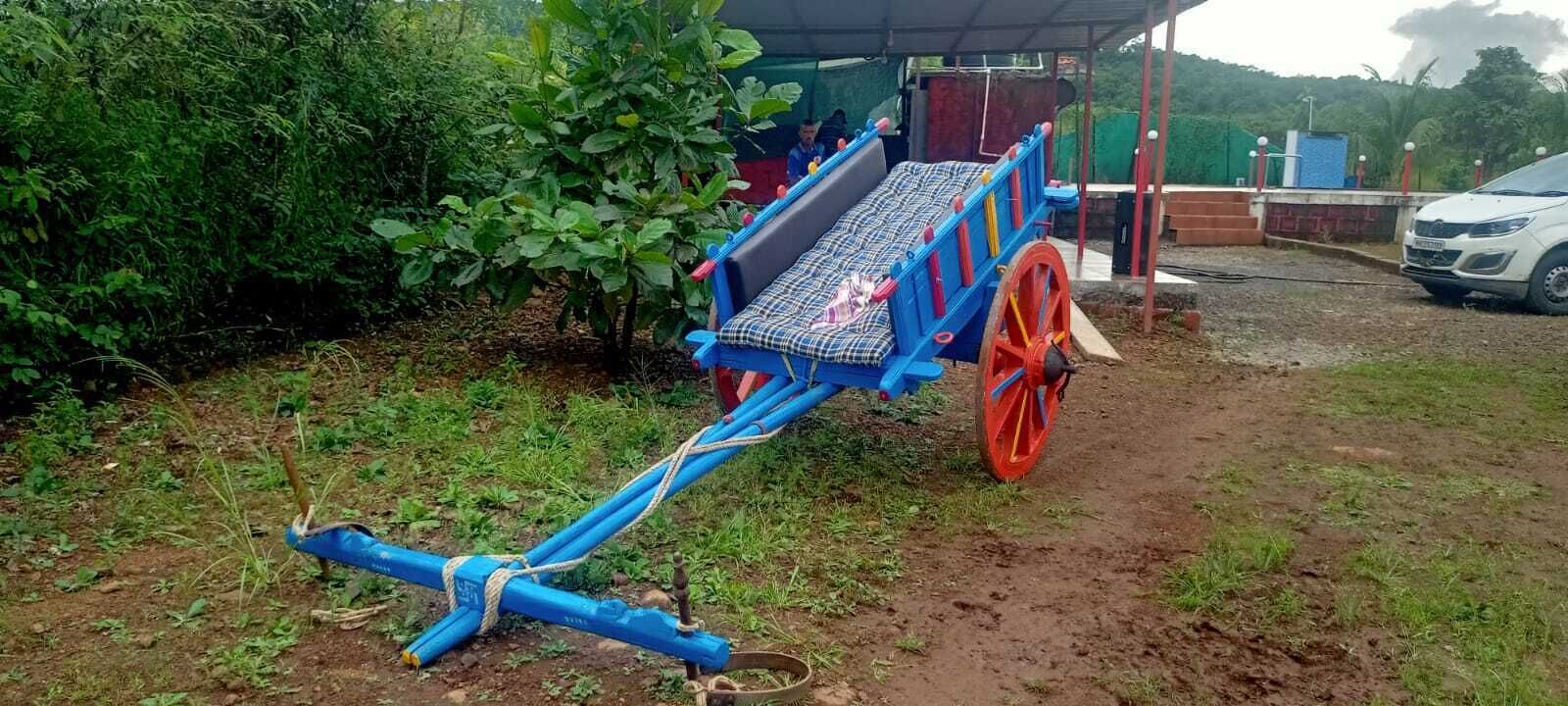 Un chariot bleu, muni d’un matelas et d’une roue rouge, est garé à l’extérieur, entouré de verdure.