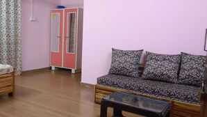 Een kamer met een houten bed, een bank met gestreepte kussens, een glazen salontafel en een roze garderobe.