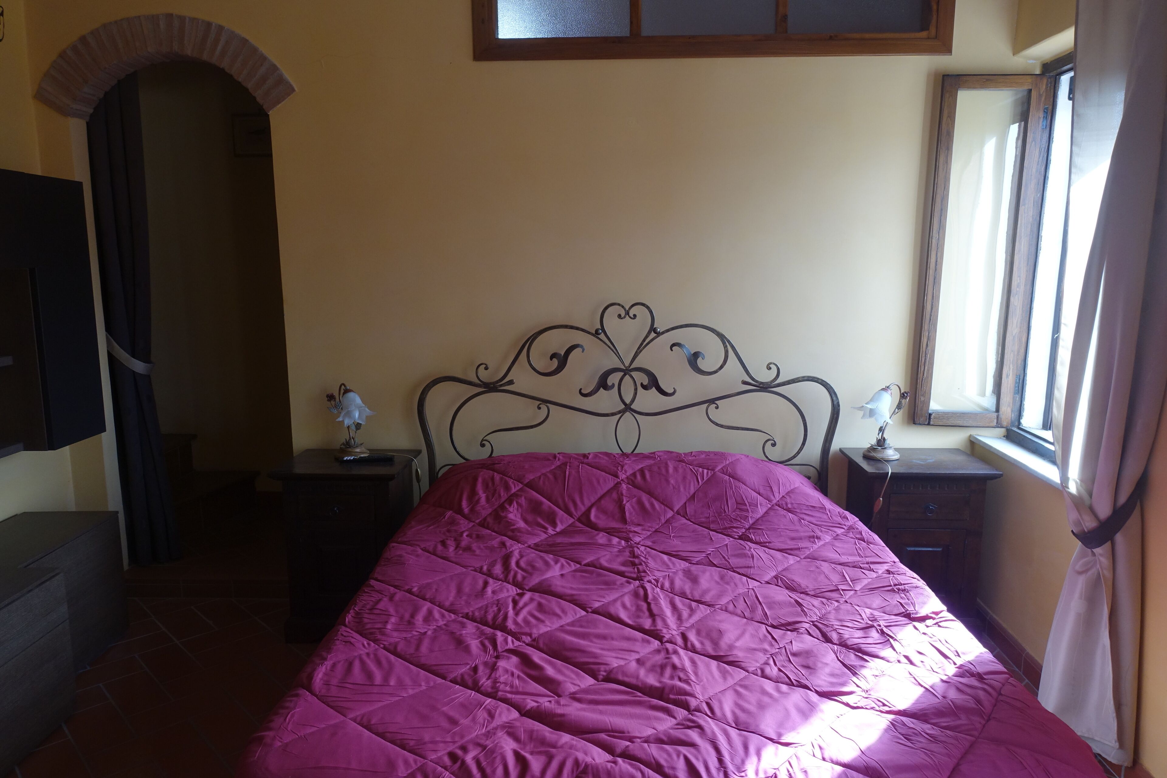 Ein Schlafzimmer mit einem Bett, einem Schminktisch, einem Nachttisch, einem Spiegel und einem Fenster mit Vorhängen.