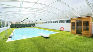 A pool area with a glass ceiling, artificial grass, and a small wooden structure. - Spa Home With Swimming Pool, Hottub, and Sauna (Sheffield)