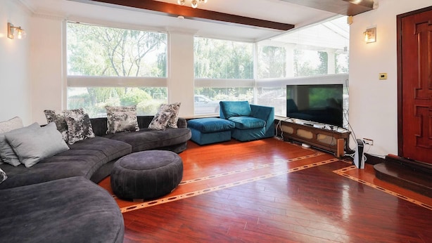 A living room with a sectional sofa, a blue armchair, and a flat-screen TV. - Spa Home With Swimming Pool, Hottub, and Sauna (Sheffield)