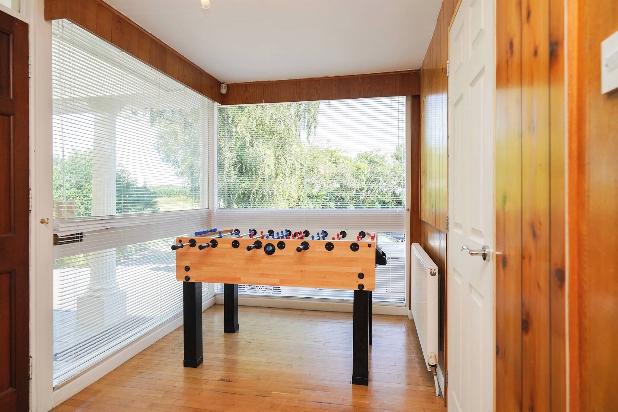 Une pièce avec une table de baby-foot, de grandes fenêtres, un plancher en bois et une porte.