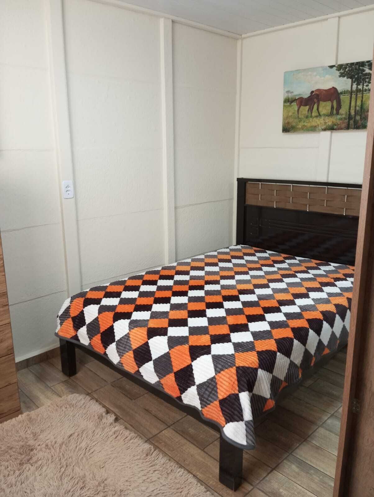 Un dormitorio con colcha a cuadros, cabecera de madera y un cuadro de caballos en la pared.